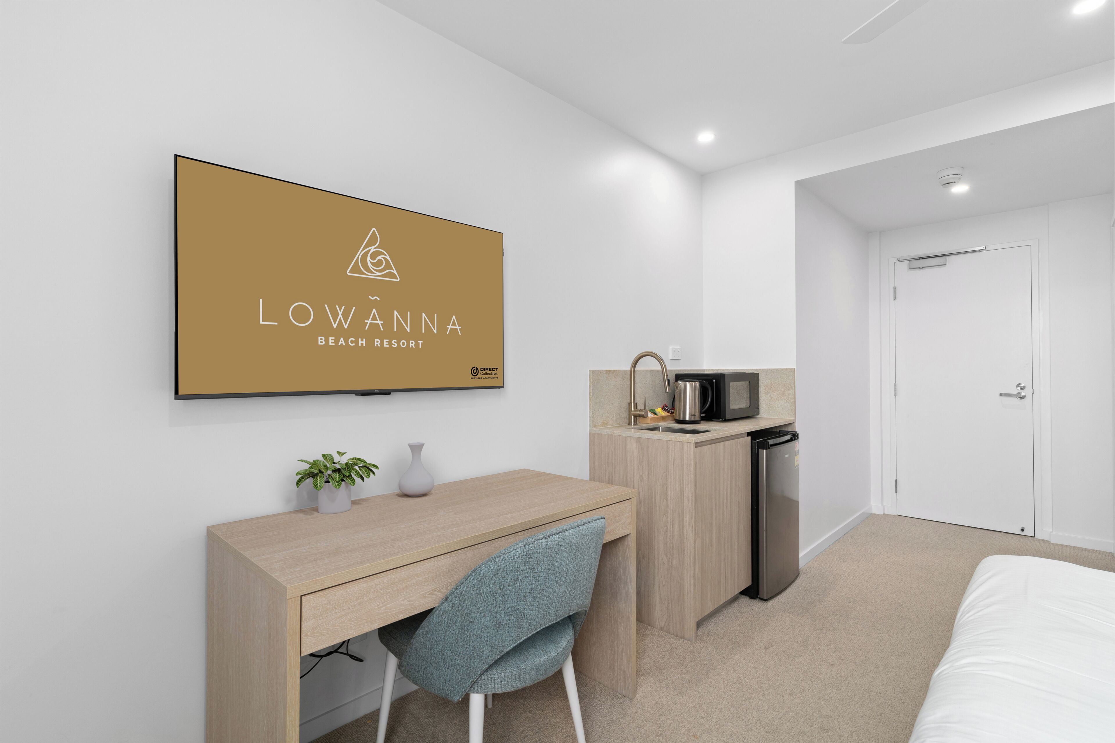 A modern hotel room with a bed, a desk with a chair, a microwave, and a small kitchenette.