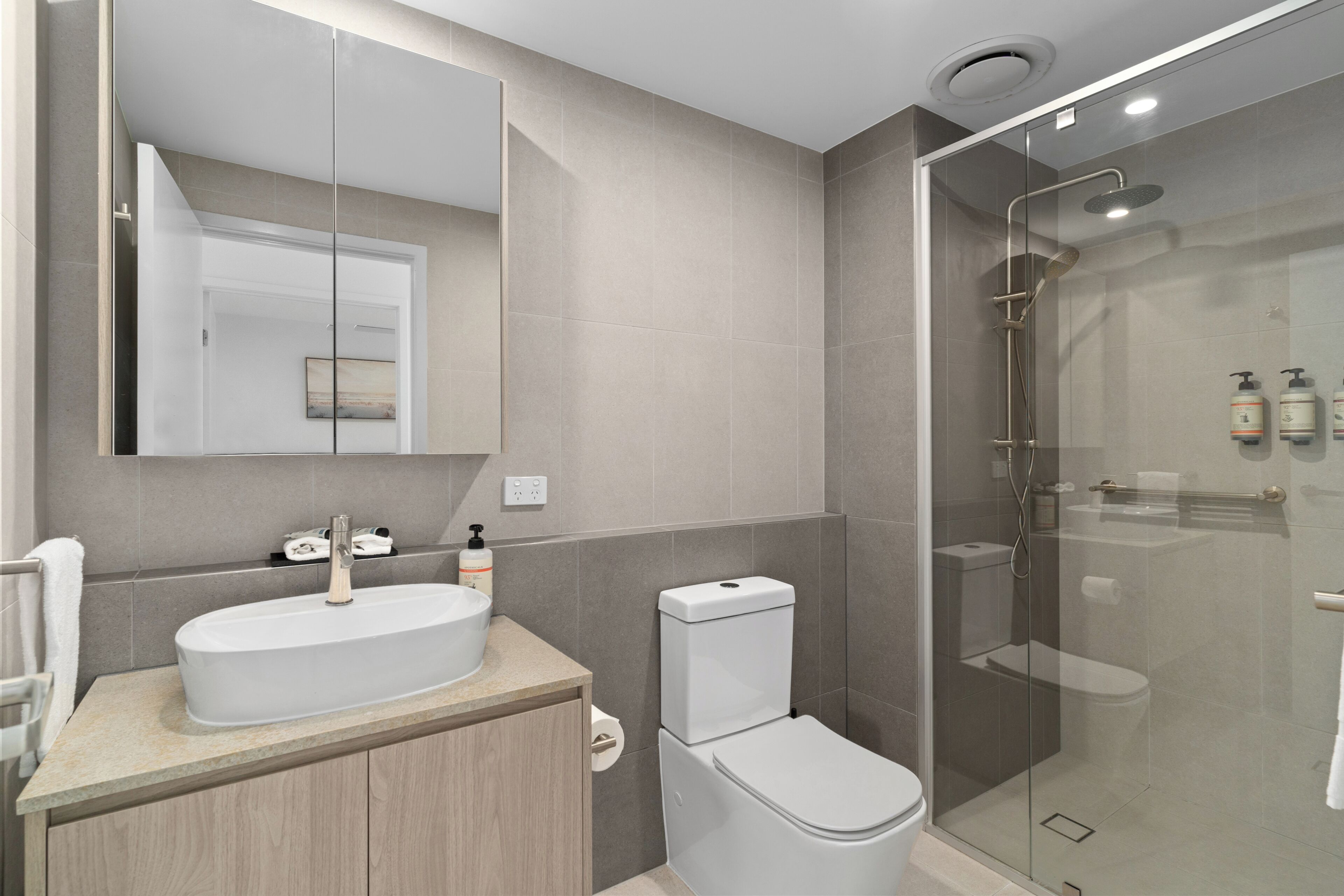 A modern bathroom with a glass-enclosed shower, a sink with a mirror, and a toilet.