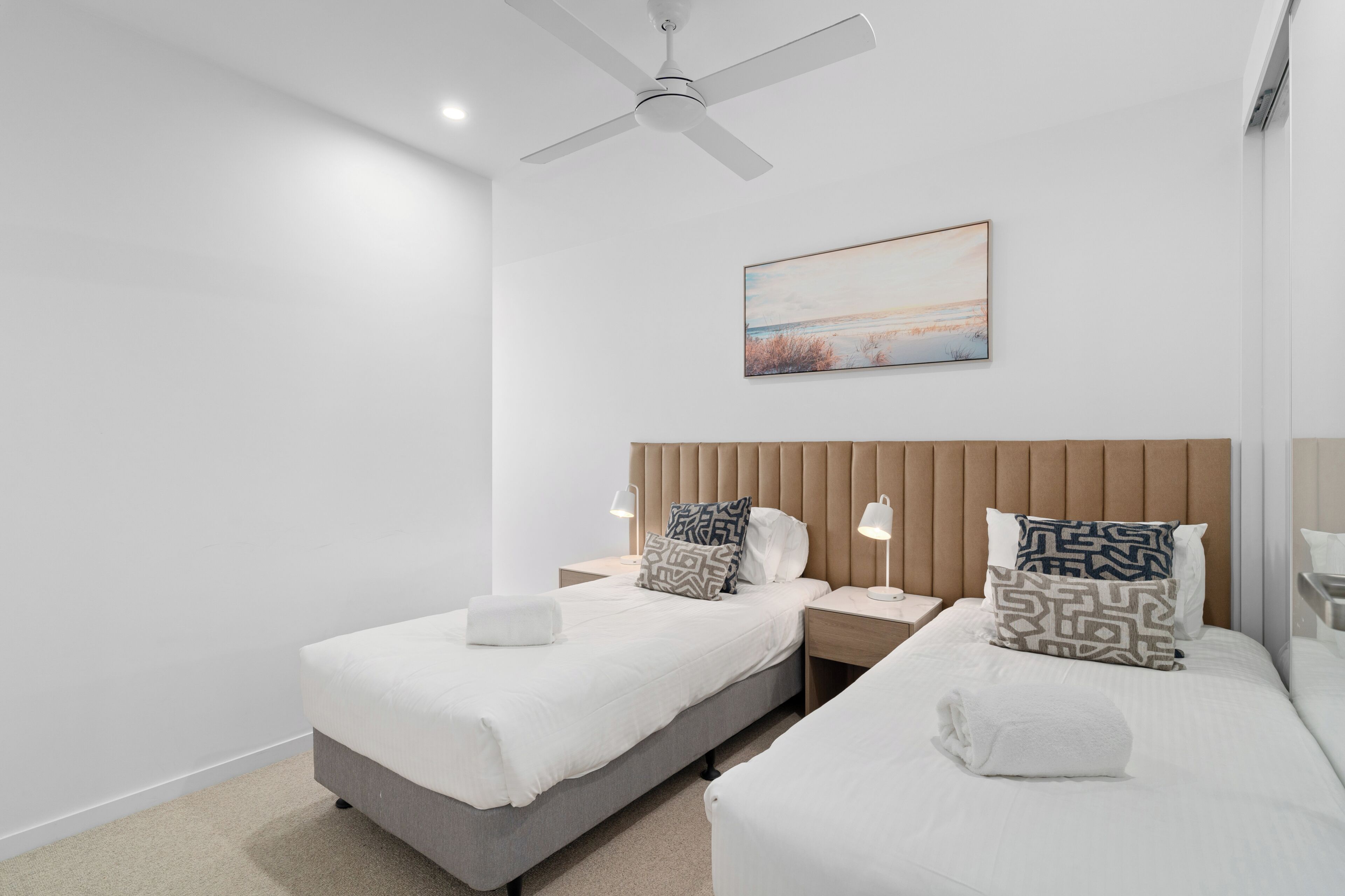 Une chambre d’hôtel moderne avec deux lits, un ventilateur de plafond, des lampes de chevet et un tableau au mur.