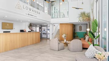 Un área de recepción moderna con un mostrador de madera, zona de estar con sofás y sillones, y una escalera que conduce a un nivel superior.