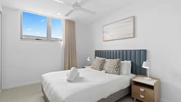 A bedroom with a bed, a nightstand, a ceiling fan, a window, and a wall-mounted artwork.