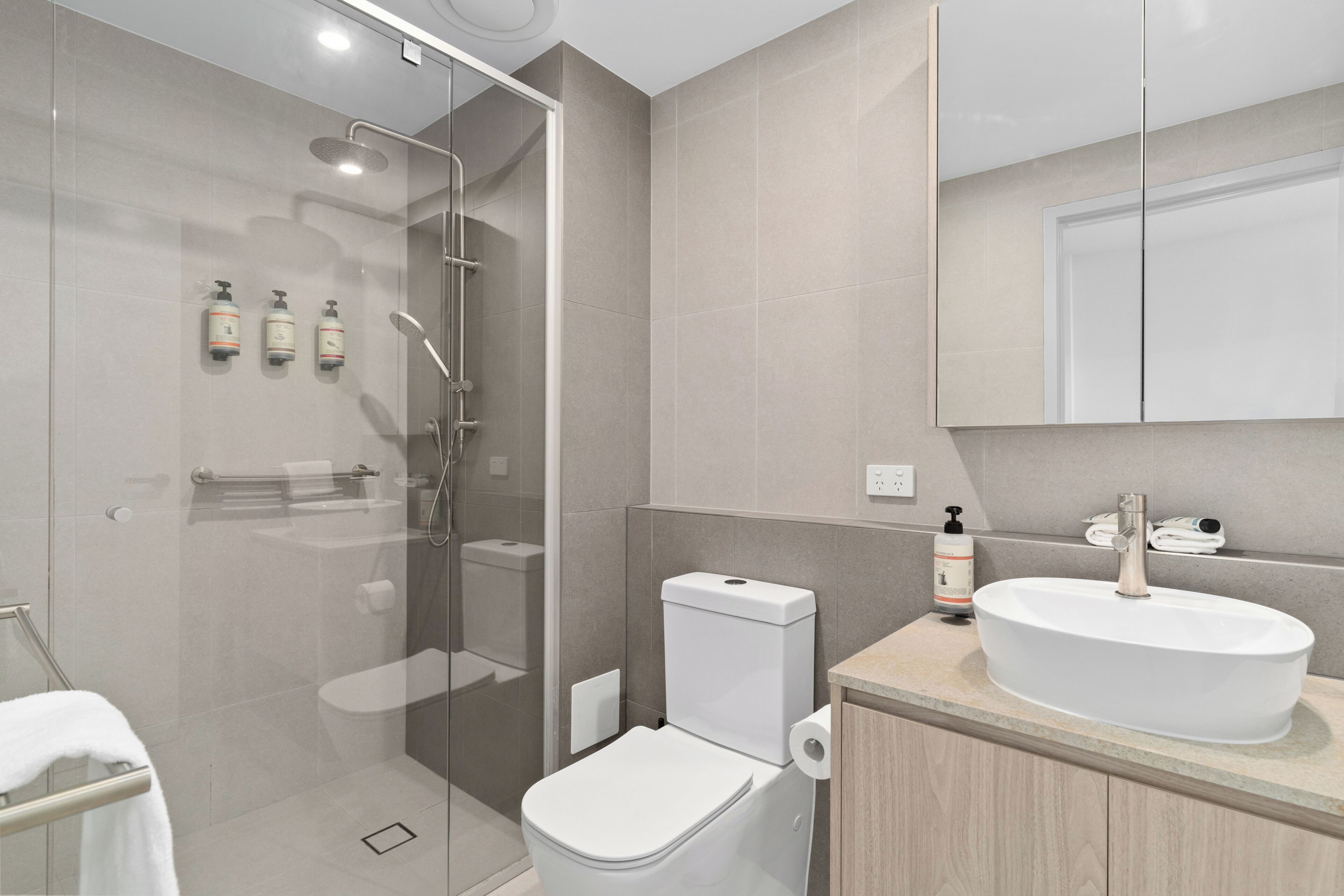 Un baño moderno con cabina de ducha de vidrio, inodoro blanco, lavabo con espejo y artículos de tocador en la pared.