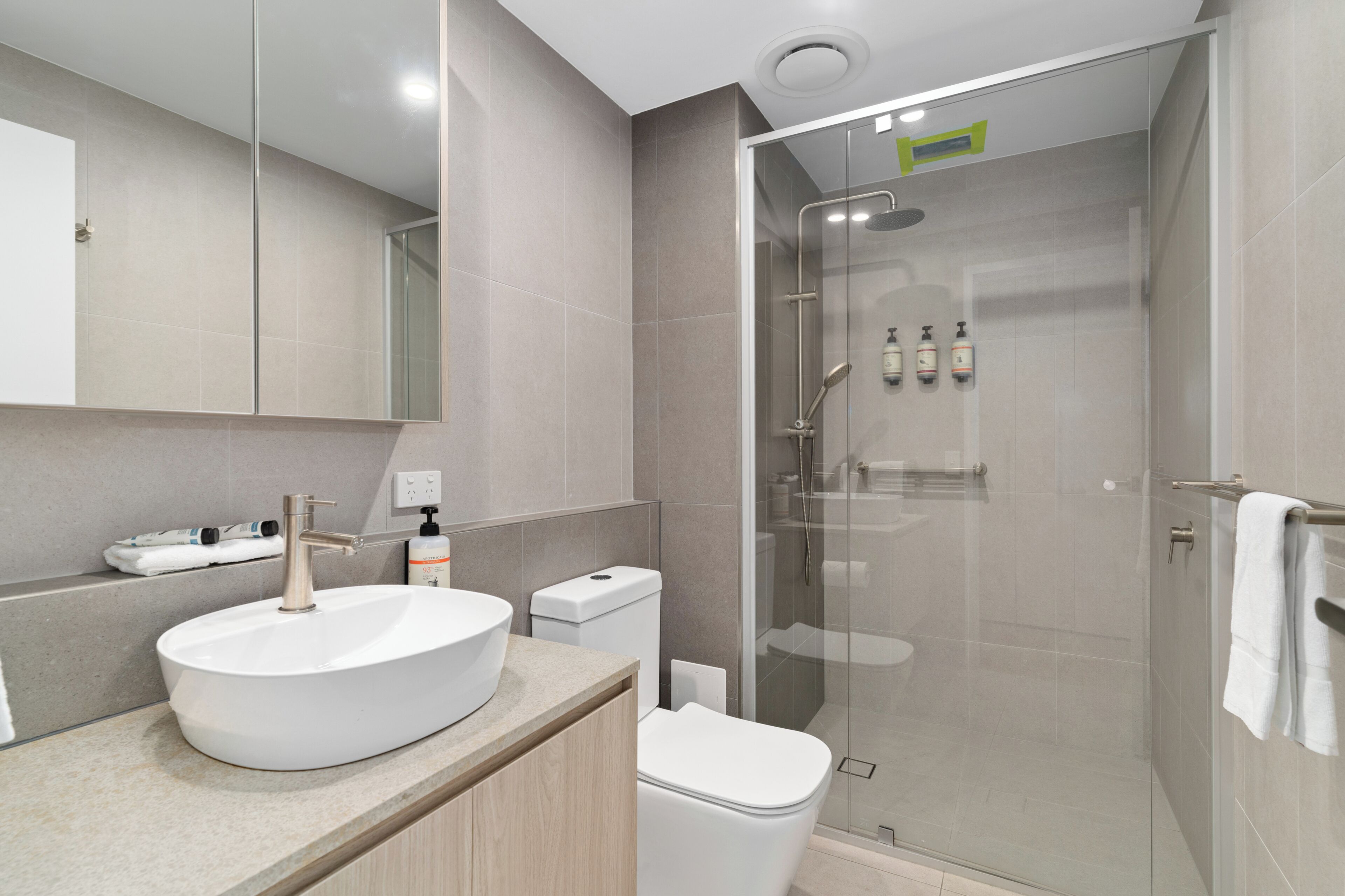 A modern bathroom with a large white sink, a toilet, and a glass-enclosed shower.