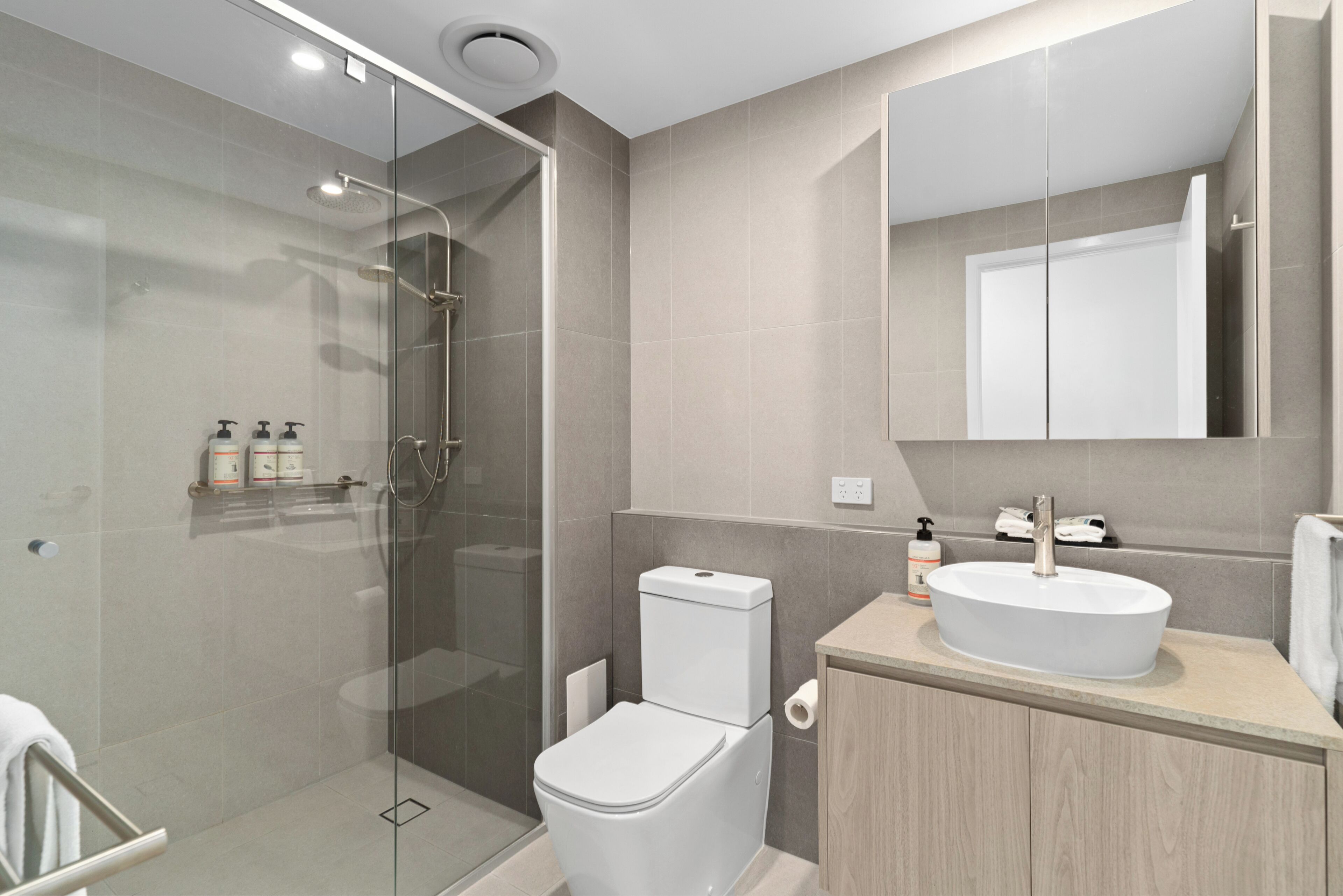 Une salle de bain moderne avec une douche à parois de verre, des toilettes, un lavabo avec un miroir au-dessus et un meuble contenant des articles de toilette.