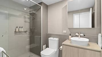 A modern bathroom with a glass-enclosed shower, a toilet, a sink with a mirror above, and a cabinet with toiletries.