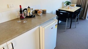 Una kitchenette con refrigerador, hervidor de agua, copa de vino y un tazón de bocadillos.