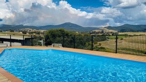 Una piscina con cubierta de madera, rodeada por una valla de metal negro, con vistas a un paisaje pintoresco con montañas y campos.