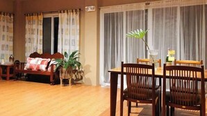 Un salon avec un plancher en bois, un canapé avec des coussins, une table à manger avec des chaises et une plante en pot.