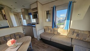 Un intérieur de camping-car compact comprenant un coin cuisine, un espace repas et un coin salon offrant une vue sur l’extérieur.