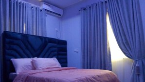 A bedroom with a large bed, a headboard, and curtains.