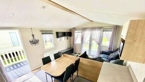 A compact living space with a dining area, a sofa, and a TV mounted on the wall. - Luxury Chichester caravan  Seaside Retreat (Chichester)