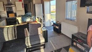 A compact living space with a kitchenette, a sofa, a small table, and a window with curtains. - Luxury Chichester caravan  Seaside Retreat (Chichester)
