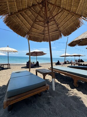 A beach with thatched umbrellas, lounge chairs, and wooden tables.