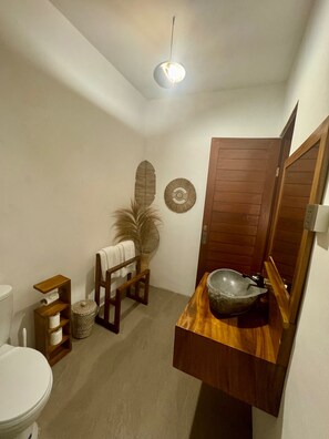 A bathroom with a wooden vanity, a large mirror, a bowl sink, a towel rack, a toilet, and decorative wall art.