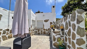 A stone-walled outdoor area with a patio, a white building with a window, and a potted plant.