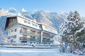A multi-story hotel with balconies, set against a snowy mountain backdrop.