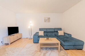 Una sala de estar con un sofá seccional azul, un televisor sobre un mueble de madera, una lámpara de pie y una alfombra con diseño de mármol.