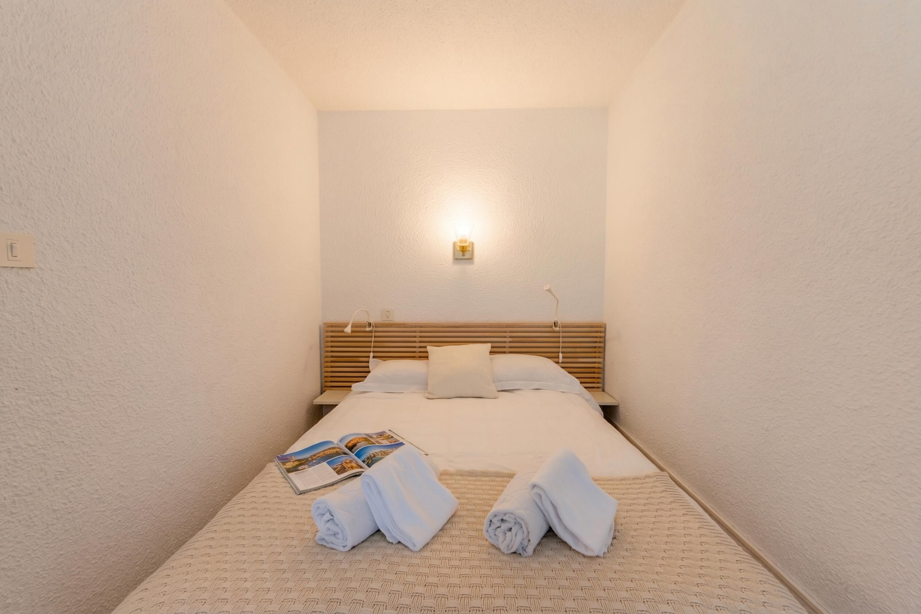 A hotel room with a bed, a nightstand, a lamp, and towels on the bed.