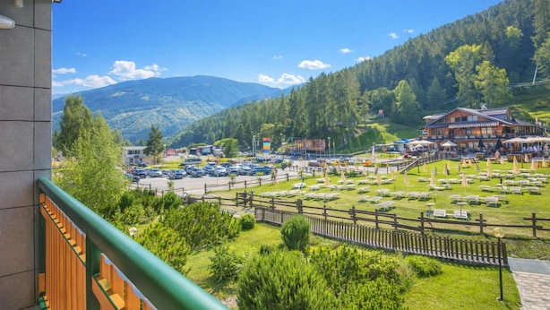 Hotel met uitzicht op een parkeerplaats, een restaurant en een bergachtig landschap.