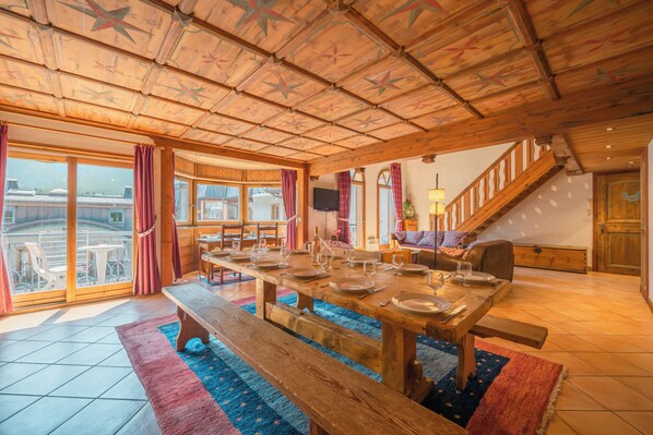 Ein geräumiger Essbereich mit einem großen Holztisch, gedeckt für eine Mahlzeit, einer Bank und einer Treppe, die zu einer oberen Ebene führt.