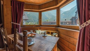 Una mesa de madera para comer con sillas, un banco y un ventanal con vistas a la montaña.
