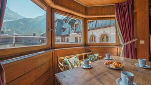 Una cabaña de madera con una mesa lista para el desayuno, una ventana con vistas a las montañas y un balcón con barandilla.
