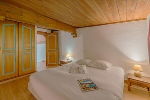 A bedroom with a wooden ceiling, a bed with white linens, a magazine on the bed, and a nightstand with a lamp.