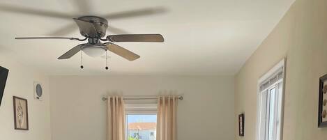 Una camera da letto con un letto, una ventola a soffitto, una finestra con tende e vista sul verde circostante.