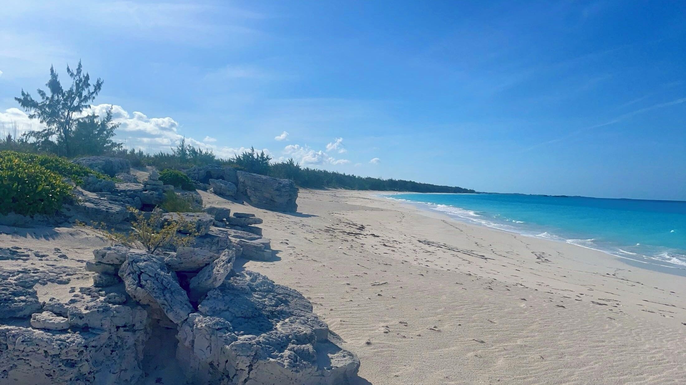 A beach with clear blue water, sandy shore, and rocky outcrops.