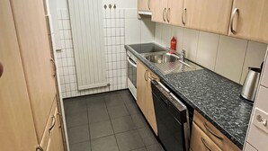 A kitchen with wooden cabinets, a black countertop, a stainless steel sink, and a dishwasher.