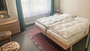 A bedroom with a bed, a nightstand, a dresser, a mirror, and a window with curtains.