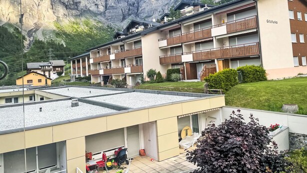 A multi-story hotel with balconies, set against a mountainous backdrop.