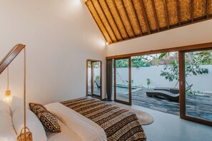 A modern bedroom with a large bed, a hanging light fixture, and a view of an outdoor pool area. - Villa Diamond  (Lembongan Island)