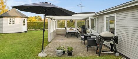 A patio area with a table and chairs, a grill, and a large umbrella.