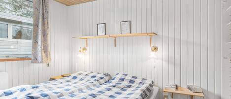 A bedroom with a wooden ceiling, two beds with checkered bedding, a window with curtains, and wall-mounted light fixtures.