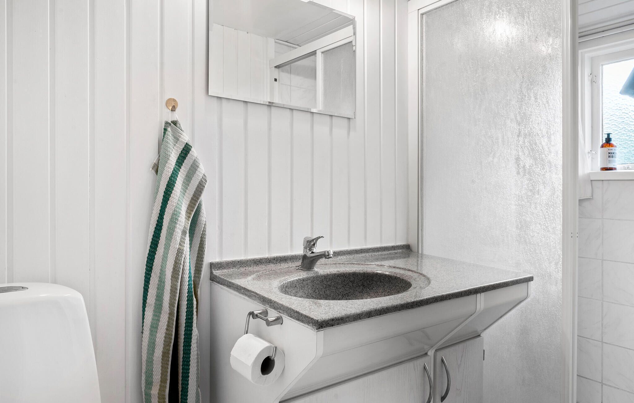 A bathroom with a granite sink, a towel rack with a striped towel, a toilet paper holder, and a window with a view of the sea.
