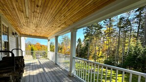 Une terrasse en bois avec des rampes blanches, donnant sur une zone boisée.