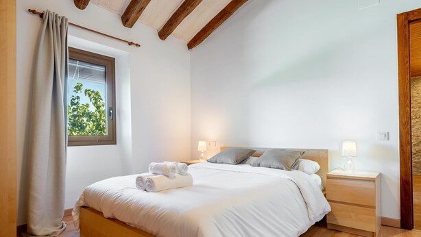 Une chambre à coucher avec un lit en bois, deux tables de chevet avec des lampes, une fenêtre avec des rideaux et une vue sur la verdure à l’extérieur.