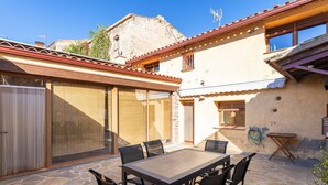 Une terrasse avec une table et des chaises, un espace couvert et un bâtiment doté d’un toit en tuiles.