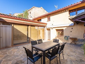 Une terrasse avec une table et des chaises, un espace couvert et un bâtiment doté d’un toit en tuiles.