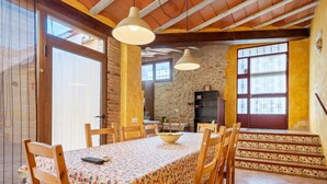 Un coin repas avec une table dressée pour six personnes, des chaises en bois, une nappe à motifs et un luminaire suspendu.