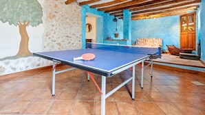Une table de ping-pong dans une pièce dotée d’un plafond rustique, d’un mur en pierre orné d’une fresque représentant un arbre et d’un mur bleu avec une armoire en bois.
