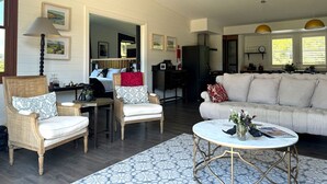 Ein geräumiges Wohnzimmer mit einer Couch, zwei Sesseln, einem Couchtisch und einem Essbereich, mit einer Küche im Hintergrund.
