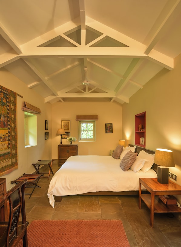 Ein Schlafzimmer mit einem großen Bett, einem Nachttisch aus Holz, einem Schreibtisch, einem Stuhl, einem roten Regal, einem Fenster und einem Deckenventilator.