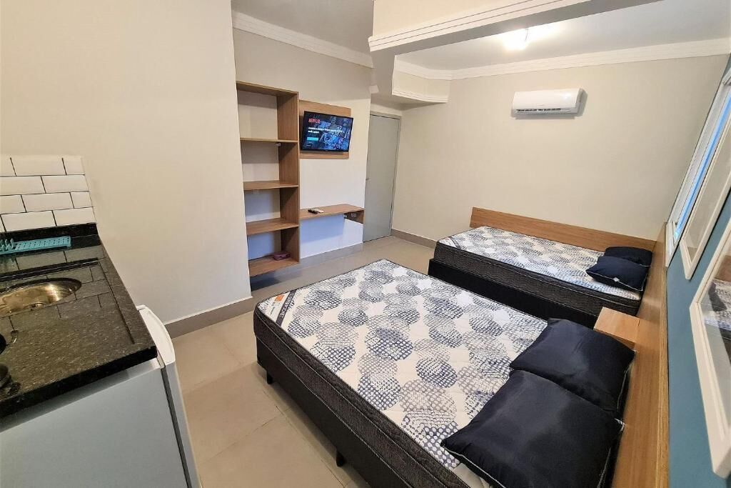 Une chambre de taille modeste équipée de deux lits, d’une kitchenette, d’un téléviseur et d’un appareil de climatisation.
