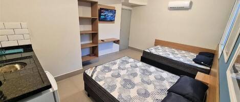 Une chambre de taille modeste équipée de deux lits, d’une kitchenette, d’un téléviseur et d’un appareil de climatisation.