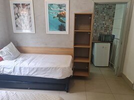 Un dormitorio con una cama, una estantería de madera, un refrigerador pequeño y dos cuadros en la pared.