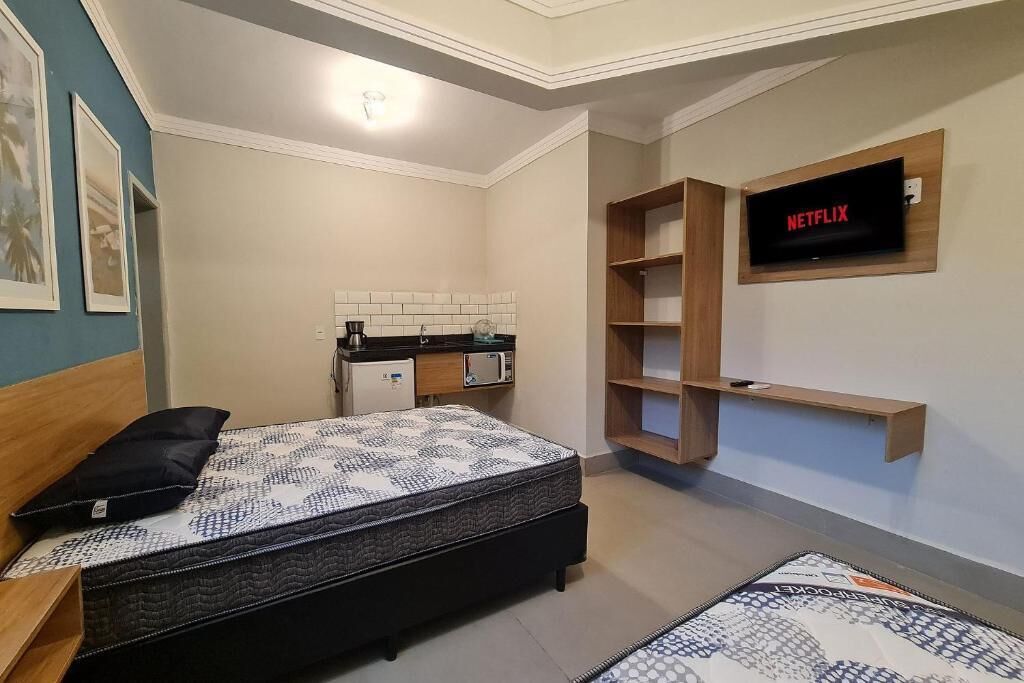 Une chambre avec un lit, un téléviseur fixé au mur et un coin cuisine.
