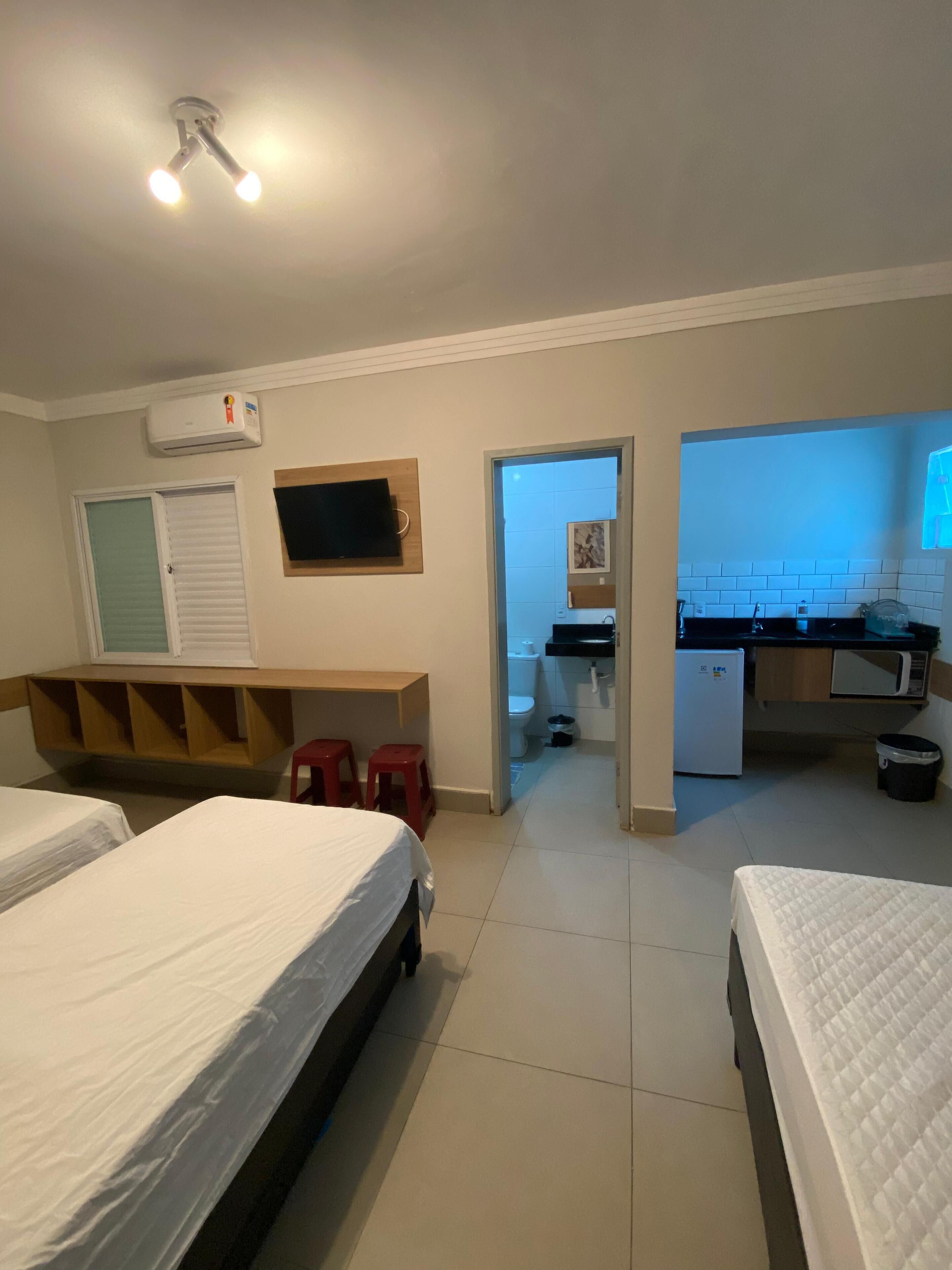 A room with two beds, a desk, a TV, and a kitchenette.