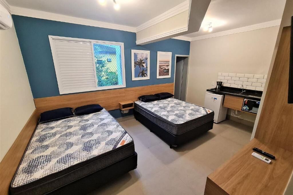 A compact room with two beds, a small kitchenette, and a window with blinds.